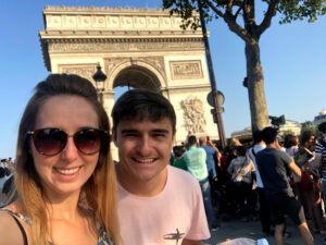 Homem usando camiseta rosa e mulher com óculos escuros na frente do arco do Triunfo