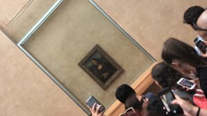 Quadro da Monalisa ao fundo com cabeça de pessoa na frente e um celular